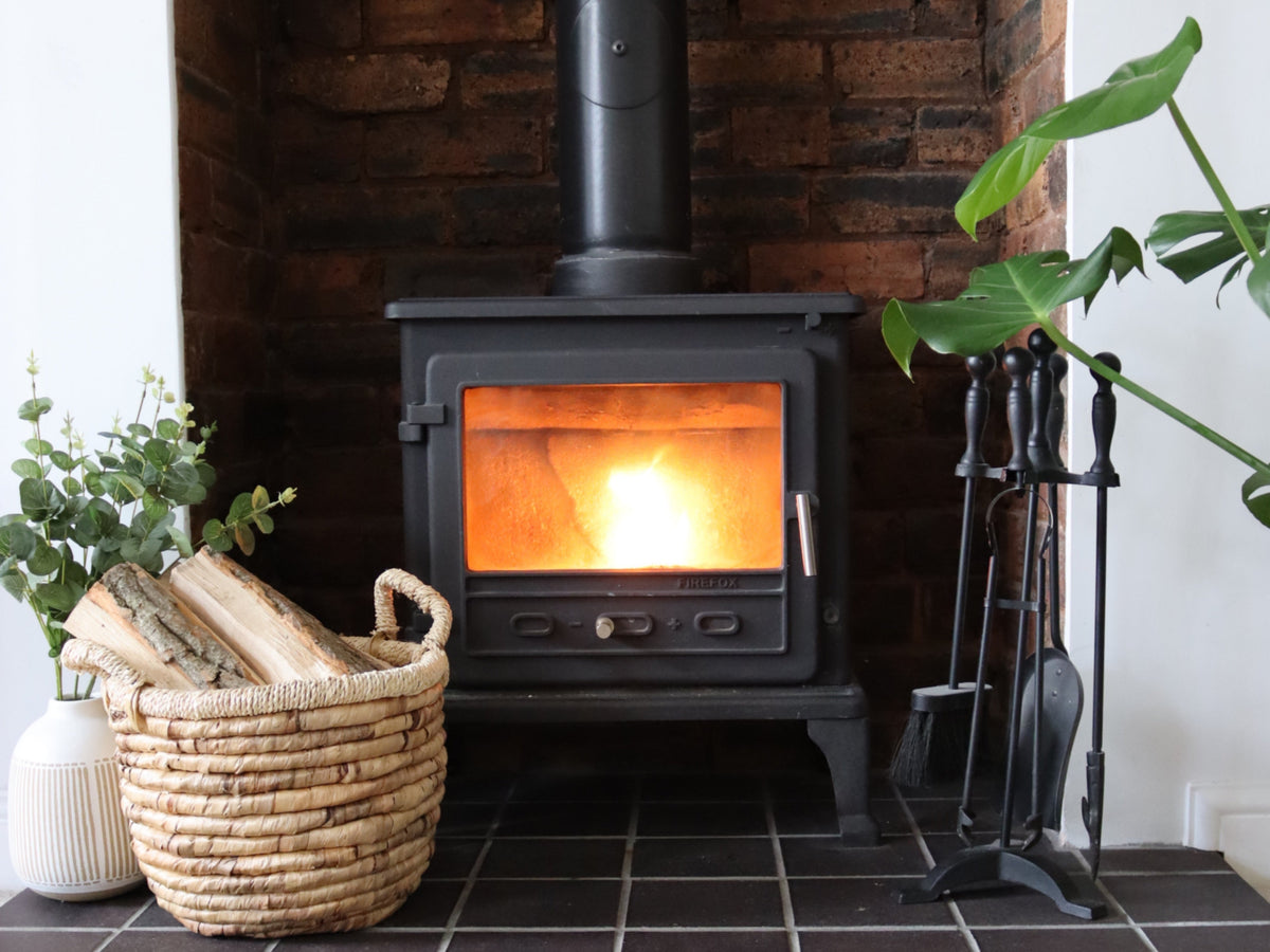 A Log burner with wood next to it and a blazing fire inside