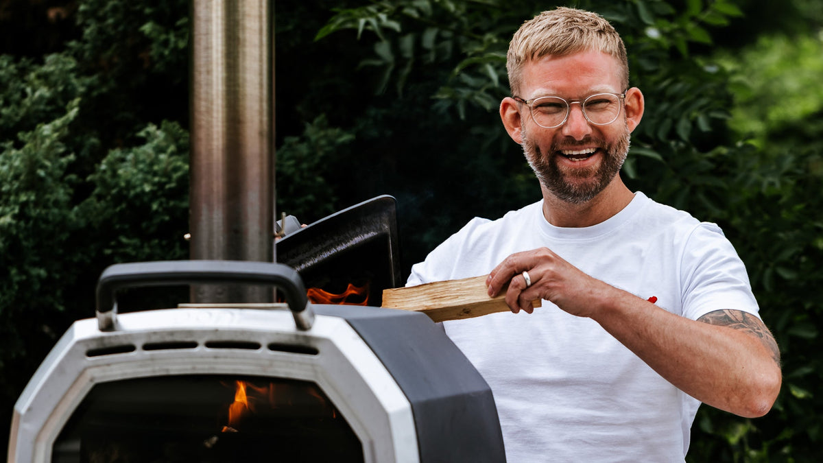 A man putting wood into he back of the Ooni Karu 16