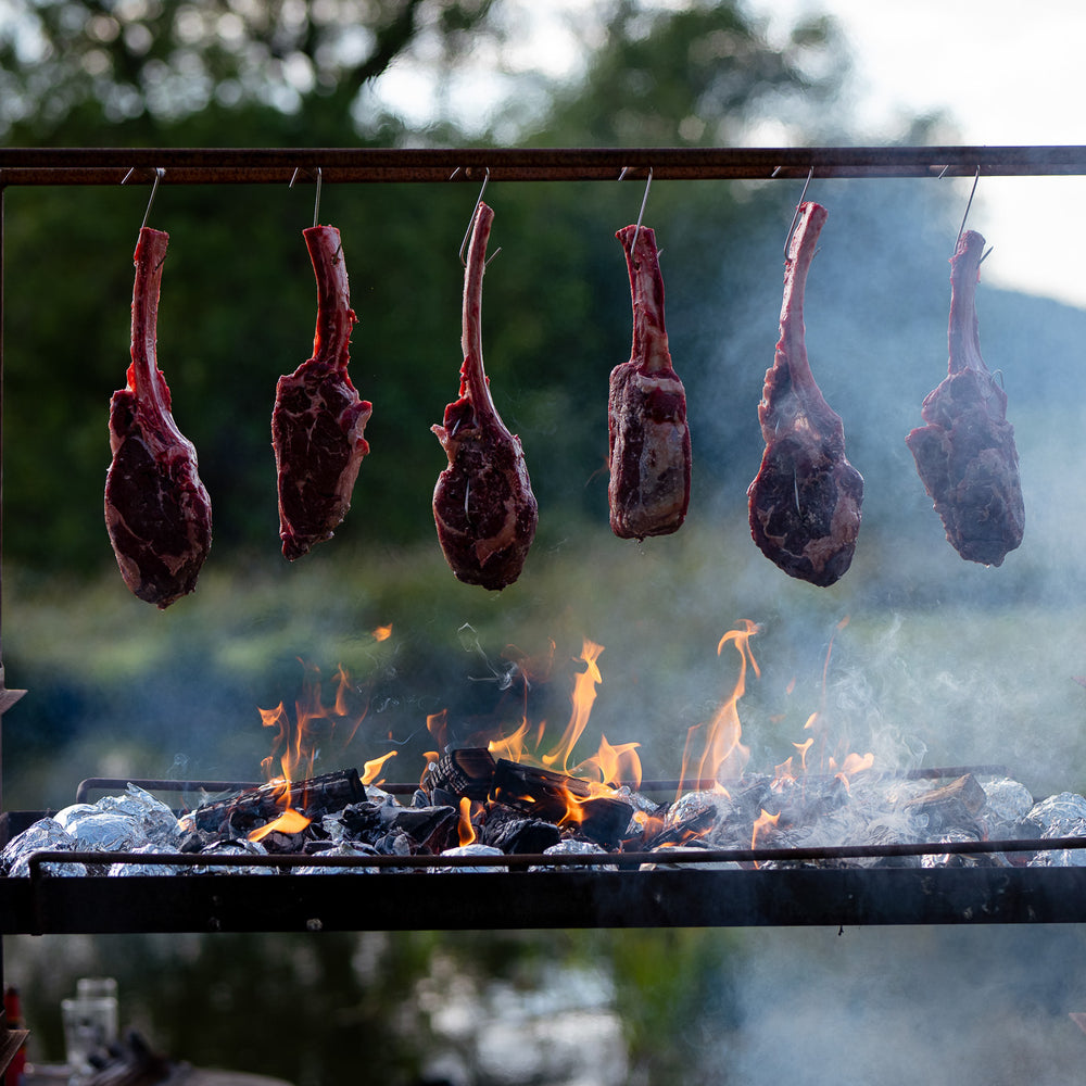 Tomahawk steaks hanging over a wood fire