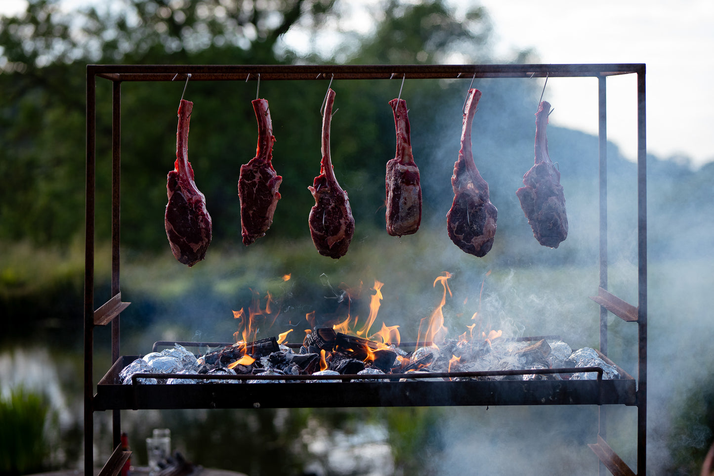 Tomahawk steaks hanging over a wood fire